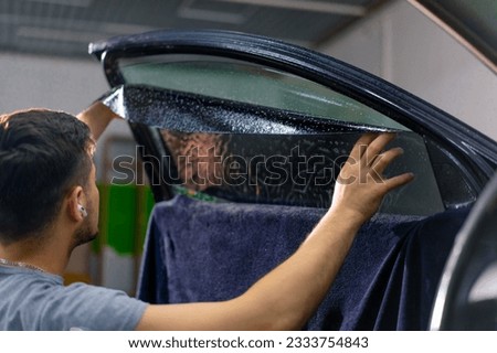Male car service worker glue window tinting in luxury car detailing car repair the concept of love for cars and protection Royalty-Free Stock Photo #2333754843