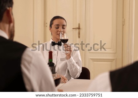 Group of people tasting red wine in glasses at table indoors, space for text. Professional butler courses