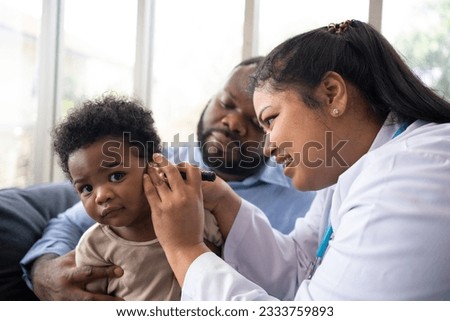 Pediatric doctor examining ear for a hearing test examining cute little girl in medical healthcare hospital or clinic. Smiling African American Baby whit pediatrician in hospital