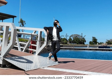 Portrait of asian rich man standing near expensive yachts, looking away outdoors. Attractive indonesian male posing for picture at marina boom beach banyuwangi