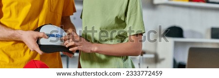 Cropped view of young african american craftswoman holding printing layer near colleague with snapback and laptop in print studio, small business resilience concept, banner
