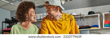 Young and positive multiethnic craftspeople talking and looking at each other while working together in blurred print studio at background, thriving small enterprise concept, banner