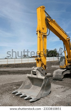 Steel excavator bucket on a yellow industrial digger, standing idle on a building site.