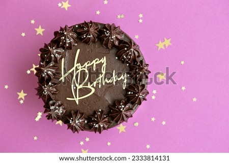 Chocolate birthday cake with gold happy birthday lettering against a pink background, overhead view