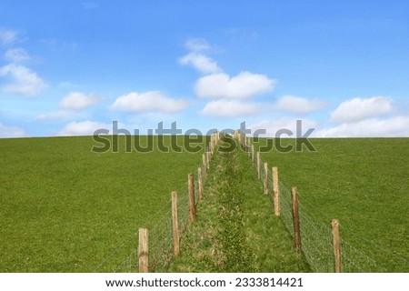 Double wooden post and wire fence line dividing a field. Set against a blue sky with alto cumulus clouds.