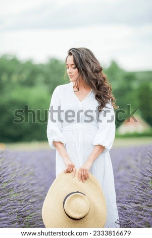 Lavender field. Beautiful dark-haired curly woman in white simple dress in field of purple flowers.
