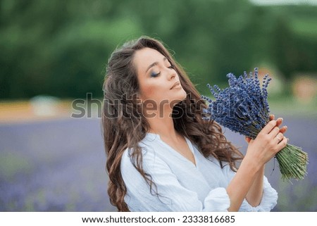 Lavender field. Beautiful dark-haired curly woman in white simple dress in field of purple flowers.