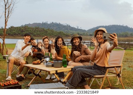 Hilarious group selfie action with male and female besties together waved hello tabletop selfies camping taking photos with smartphones. Fun holidays vacation in forests and mountains at sunset.
