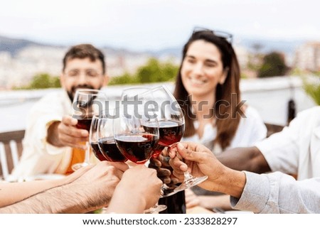 Young group of people drinking red wine at rooftop summer party in the evening. Reunited millennial friends celebrating together at home garden.