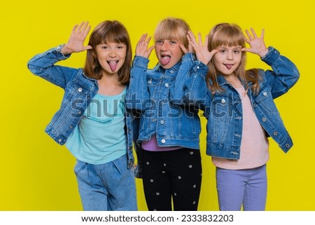 Funny happy teenage girls making playful silly facial expressions and grimacing, fooling around, showing tongue. Little children sisters. Three cute siblings kids isolated on studio yellow background