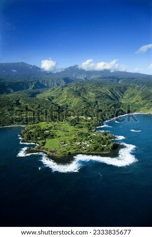 Aerial of rocky coast on Pacific ocean with mountains in background in Maui, Hawaii.