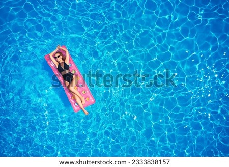 Fit pretty girl in bikini chilling on inflatable pink mattress in swimming pool. Slim hot woman in swimwear tanning. Female relaxing on float in blue water at luxury resort. Aerial, view from above. Royalty-Free Stock Photo #2333838157