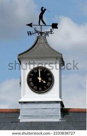 Golf weather vane with white clock tower beneath with time set at four o-clock. Set against a blue sky and clouds.