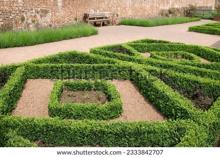 Geometric diamond shaped hedge designs within a walled red brick garden with plants inside the hedged areas and lavender borders to the rear.