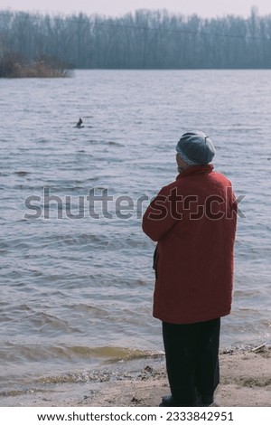 A woman in a red coat feeds ducks on the background of a river