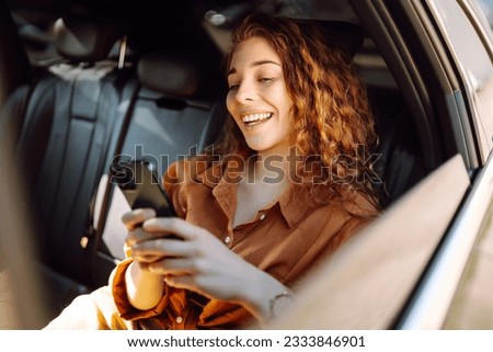 Smiling woman using smartphone while sitting in the back seat of a car. Young woman checks mail, texts, blogs in the car. Business, technology concept. Royalty-Free Stock Photo #2333846901