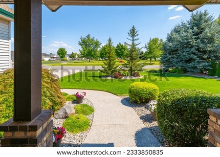 View from the front porch of a modern suburban home with a manicured front lawn in a nice community neighborhood across the street to a park on a sunny summer day. Royalty-Free Stock Photo #2333850835