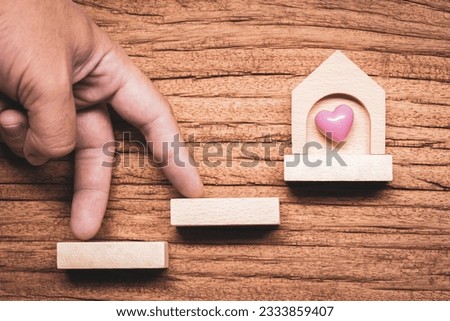 Hand with climb up on the staircase step to success with home as destinations on wood background, Investment victory to business of real estate and save money for buy the house in the future concept.