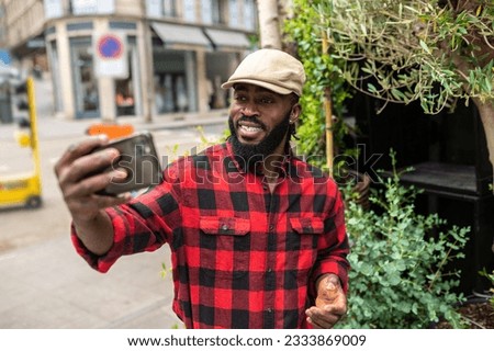 Man in a red plaid shirt making a selfie on a greenery background