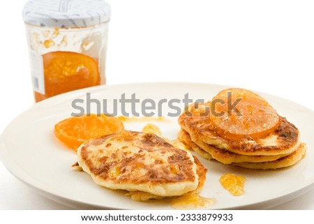 small cottage pancakes with some orange jam, jam jar in background, isolated on white