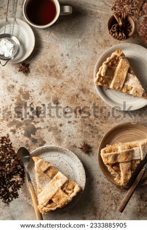 Three plates with traditional apple pie pieces served for an autumn cozy tea party with copy space on brown textured background. Autumn seasonal food concept, top view. Vertical