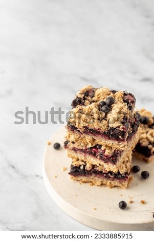Stack of baked oatmeal squares with fresh blueberry on white tray on marble background with text space. Vertical, recipe