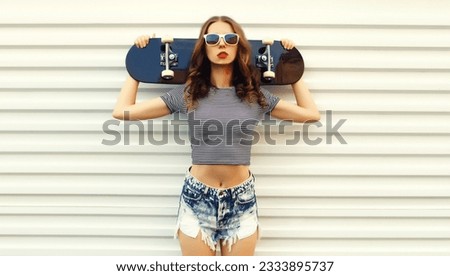 Portrait of stylish young woman with skateboard on white background