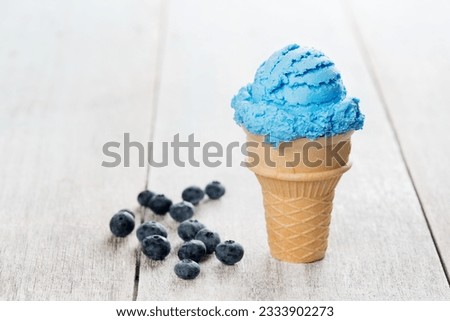 Blue ice cream in waffle cone with blueberry fruit on white rustic wooden background.