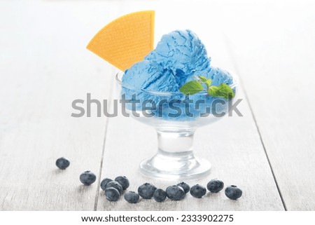 Blue ice cream in glass with blueberry fruits on white rustic wooden background.