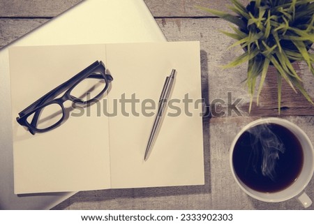 Work desk with laptop computer, diary book, pen, eyeglasses and hot coffee cup. Top view rustic wooden table background with copy space in vintage toned.