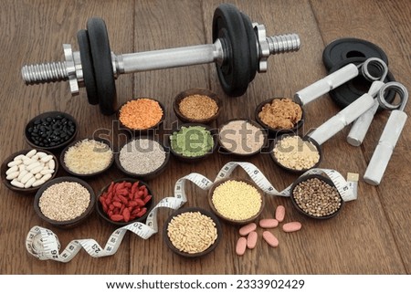 Body building equipment with dumbbells and hand grippers with health and super food of whey protein, red maca and wheat grass supplement powders, ginseng vitamin pills, pulses, seeds, nuts, grains and