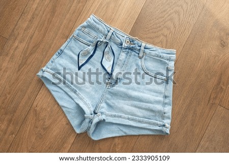 Cute elegant denim shorts with a ribbon on the belt, wooden background. Front view, top view