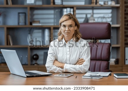 Portrait of serious mature woman inside office at workplace, businesswoman thoughtfully in glasses looking at camera with arms crossed.