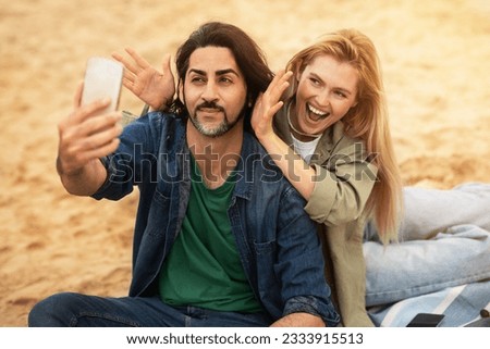 Cheerful Young Man And Woman Taking Selfie On Smartphone Outdoors And Fooling, Happy Millennial Couple Having Fun Together Outside, Relaxing With Mobile Phone On Beach Near Sea, Closeup