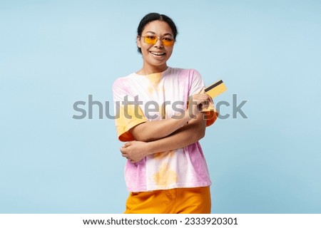 Portrait of young smiling African American woman holding credit card isolated on blue background. Happy stylish female ordering food. Technology concept 