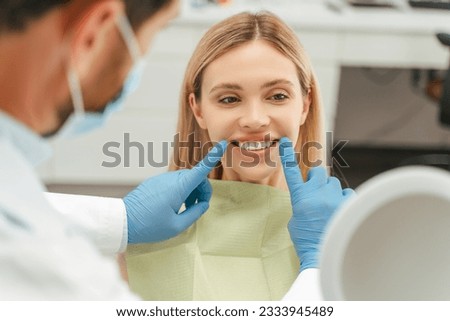Portrait of beautiful smiling caucasian woman looking in mirror, checking her teeth in modern mental clinic. Health care concept  Royalty-Free Stock Photo #2333945489