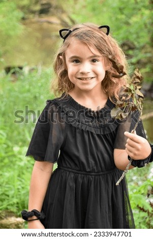 Young girl wearing a black dress and cat ear head band standing in nature. 