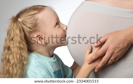 A little girl kisses the belly of her pregnant mother. The concept of motherhood and love for children.