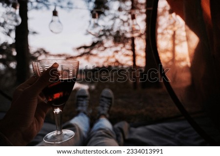 A close-up photo of the intentions of women's legs. The girl has a glass of wine or water in her hands. The concept of a tourist trekking expedition. View from the tent to the landscape.