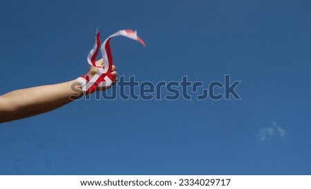 Hand wearing red and white ribbon with sky background, Indonesia independence day concept