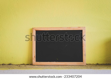 Blackboard on dirty and yellow wall in vintage style.