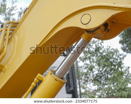 Excavator arm with hoses and hydraulic cylinders. Hydraulic system of old yellow backhoe in white cloudy sky background. Selective focus
