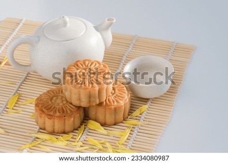 Chinese Mid-Autumn Festival concept made from mooncakes in plates and hot tea pot on bamboo mat with the white background. Chinese mid autumn festival food. 