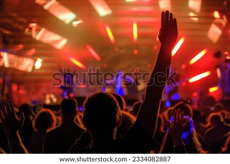 Back view of anonymous crowd of fans raising arms while dancing in concert hall and listening to cool music performance Royalty-Free Stock Photo #2334082887