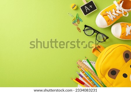 Get ready for elementary school. Top view of bear-shaped backpack, colored markers, sketchbook, art supplies, clips, glasses, A+ grade symbol, sneakers on soft green backdrop with space for text or ad