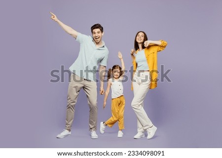 Full body young cheerful happy parents mom dad with child kid daughter girl 6 years old wearing blue yellow casual clothes raise up hands dance isolated on plain purple background. Family day concept