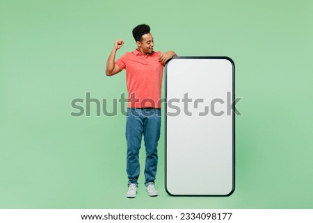 Full body fun young man he wear pink t-shirt big huge blank screen mobile cell phone smartphone with area do winner gesture isolated on plain light green background studio portrait. Lifestyle concept
