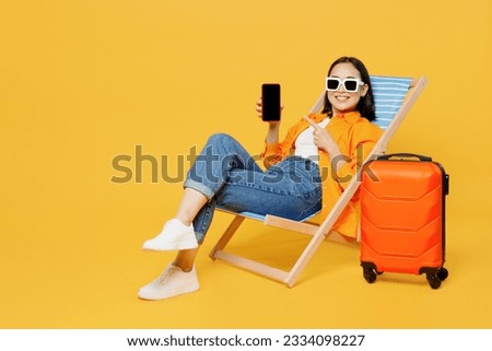Young woman wear summer clothes sit in deckchair use blank screen mobile cell phone isolated on plain yellow background Tourist travel abroad in free time rest getaway. Air flight trip journey concept