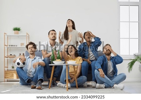 Disappointed sports fans watching letdown match on TV. Frustrated young men and women sitting on sofa at home and drinking beer. Upset friends frustrated with lost soccer game Royalty-Free Stock Photo #2334099225