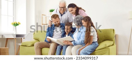 Lovely happy smiling big family with parents, kids, grandparents looking at family photo album together sitting in light living room at home, panoramic view. Emotional family moments memories concept.